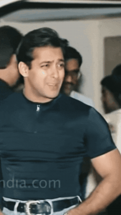 A Man In A Black Shirt Is Standing In A Crowd With India.com Written On The Bottom Left GIF