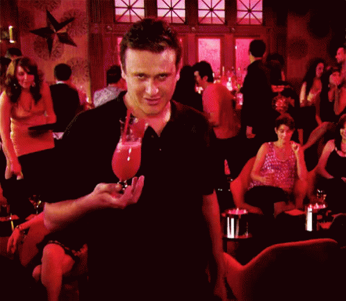 A Man In A Black Shirt Is Standing In A Crowded Bar GIF