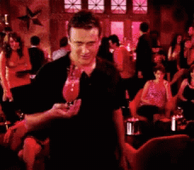 A Man In A Black Shirt Is Standing In A Crowded Restaurant Holding A Glass Of Wine GIF