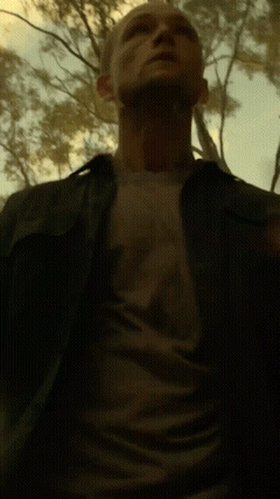 A Man In A Black Shirt Is Standing In A Dark Forest GIF