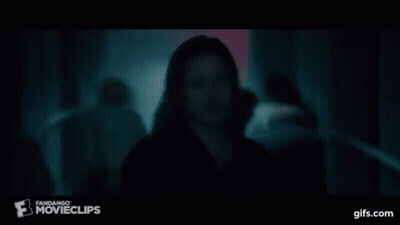 A Man In A Black Shirt Is Standing In A Dark Room In Front Of A Crowd . GIF