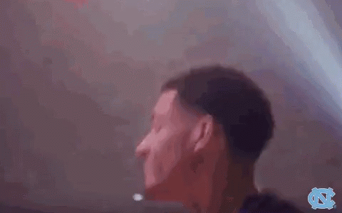 A Man In A Black Shirt Is Standing In A Dark Room With His Hands In The Air . GIF