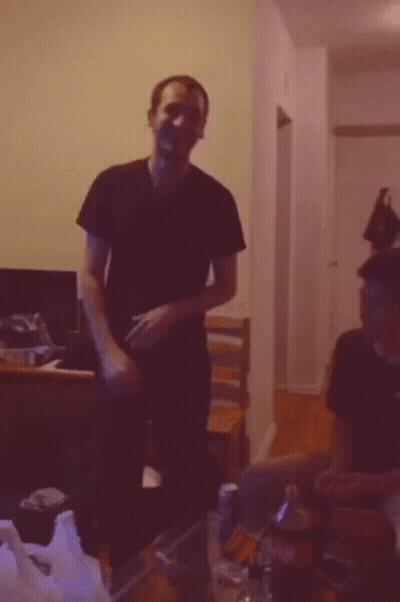 A Man In A Black Shirt Is Standing In A Dark Room GIF
