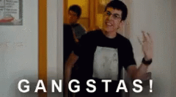 A Man In A Black Shirt Is Standing In A Doorway With The Word Gangsta Written On The Wall . GIF