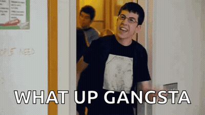 A Man In A Black Shirt Is Standing In A Doorway With The Words `` What Up Gangsta '' Written On The Bottom . GIF
