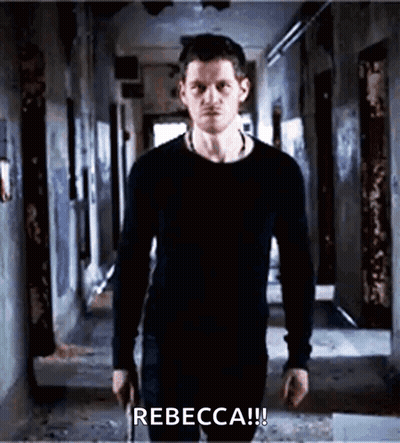 A Man In A Black Shirt Is Standing In A Hallway Holding A Gun And Says Rebecca ! GIF