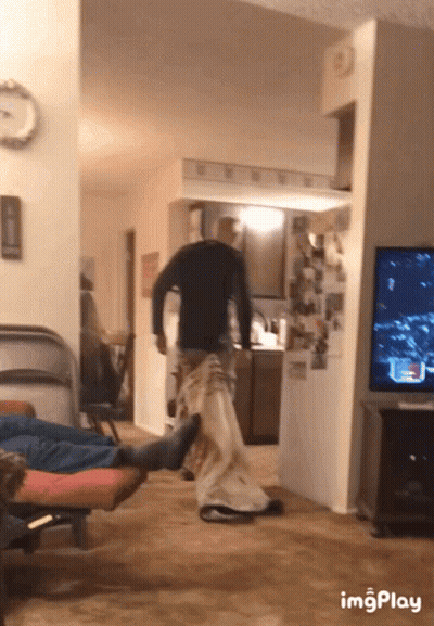 A Man In A Black Shirt Is Standing In A Living Room Next To A Tv And A Clock GIF