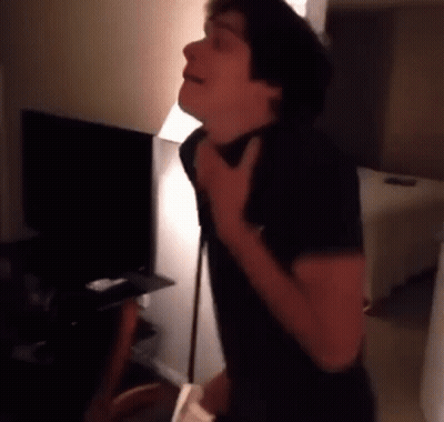 A Man In A Black Shirt Is Standing In A Living Room With His Hand On His Neck . GIF