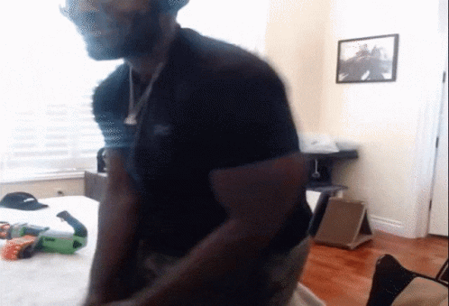 A Man In A Black Shirt Is Standing In A Room With A Picture On The Wall Above Him GIF