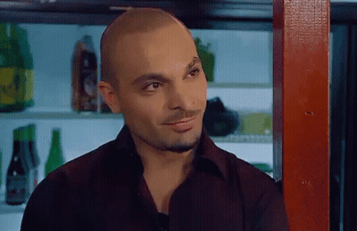 A Man In A Black Shirt Is Standing In Front Of A Bar With Bottles Of Beer On The Shelves . GIF
