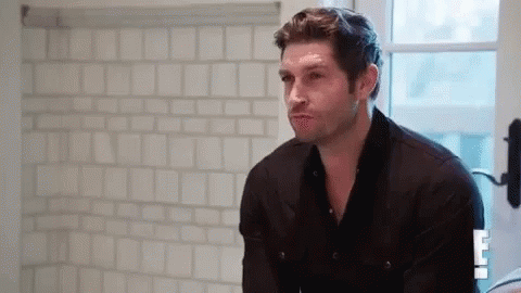 A Man In A Black Shirt Is Standing In Front Of A Bathroom Mirror . GIF