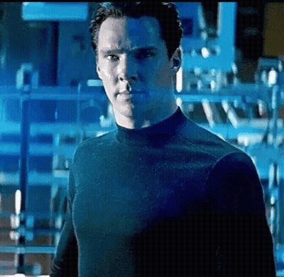 A Man In A Black Shirt Is Standing In Front Of A Blue Wall . GIF