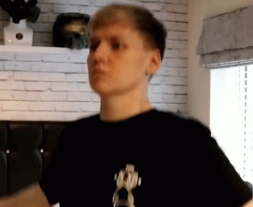 A Man In A Black Shirt Is Standing In Front Of A Brick Wall GIF