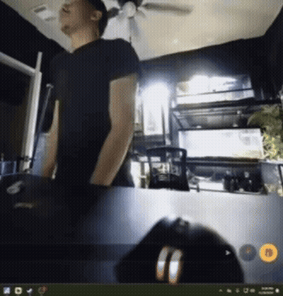 A Man In A Black Shirt Is Standing In Front Of A Computer Monitor GIF