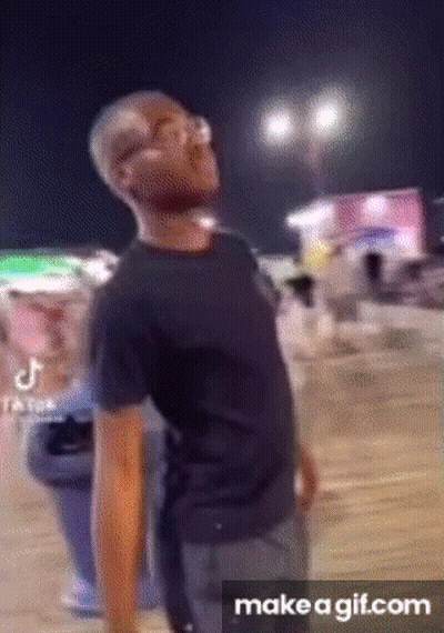 A Man In A Black Shirt Is Standing In Front Of A Crowd Of People At Night . GIF