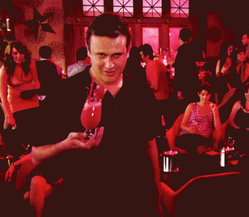 A Man In A Black Shirt Is Standing In Front Of A Crowd Of People GIF