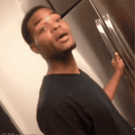 A Man In A Black Shirt Is Standing In Front Of A Fridge GIF