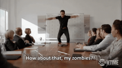 A Man In A Black Shirt Is Standing In Front Of A Group Of People And Says How About That My Zombies GIF
