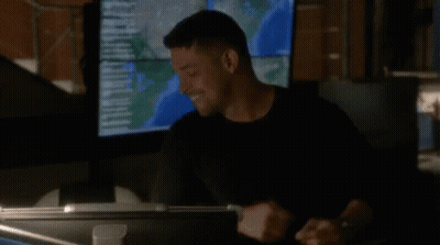 A Man In A Black Shirt Is Standing In Front Of A Large Monitor . GIF