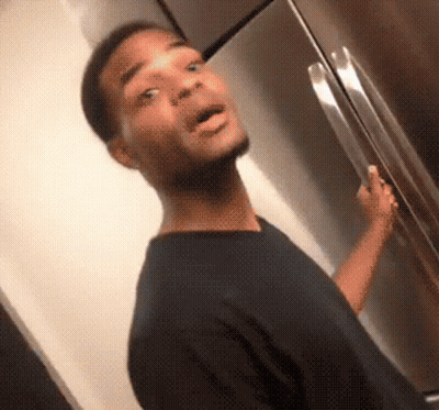 A Man In A Black Shirt Is Standing In Front Of A Refrigerator With His Mouth Open GIF