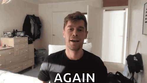 A Man In A Black Shirt Is Standing In Front Of A Sign That Says Again On It GIF