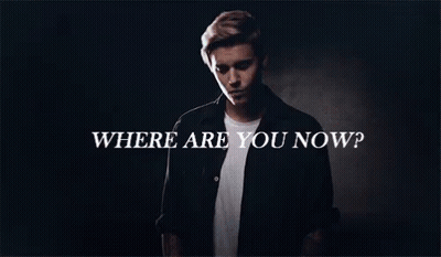 A Man In A Black Shirt Is Standing In Front Of A Sign That Says Where Are You Now GIF