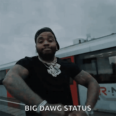 A Man In A Black Shirt Is Standing In Front Of A Train With His Hands On His Hips And Says Big Dawg Status GIF