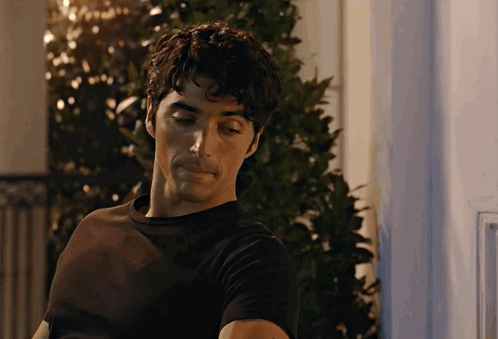A Man In A Black Shirt Is Standing In Front Of A Window GIF