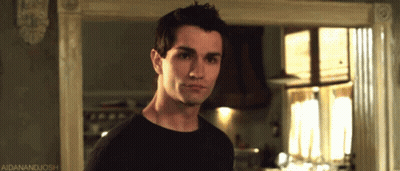 A Man In A Black Shirt Is Standing In Front Of A Window With A Caption That Says Aidanandjosh GIF