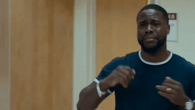 A Man In A Black Shirt Is Standing In Front Of A Wooden Door And Making A Funny Face . GIF