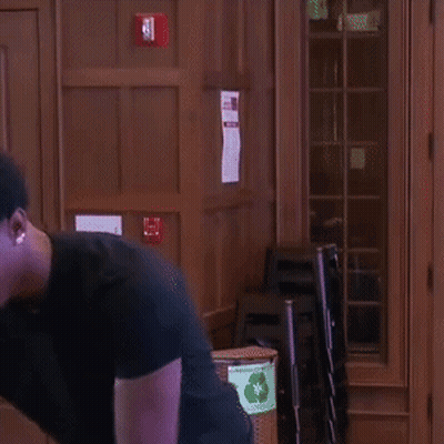 A Man In A Black Shirt Is Standing In Front Of A Wooden Door And Smiling . GIF