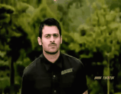 A Man In A Black Shirt Is Standing In Front Of Some Trees . GIF