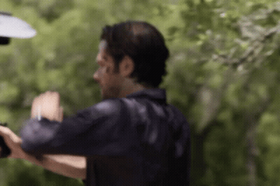 A Man In A Black Shirt Is Standing In Front Of Trees And A Lamp . GIF