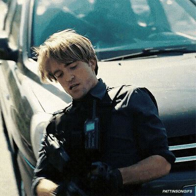 A Man In A Black Shirt Is Standing Next To A Black Car Holding A Walkie Talkie GIF