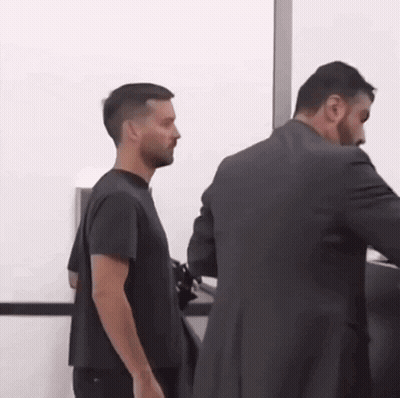A Man In A Black Shirt Is Standing Next To A Man In A Suit GIF