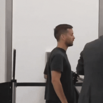 A Man In A Black Shirt Is Standing Next To A Man In A Suit At A Security Checkpoint . GIF