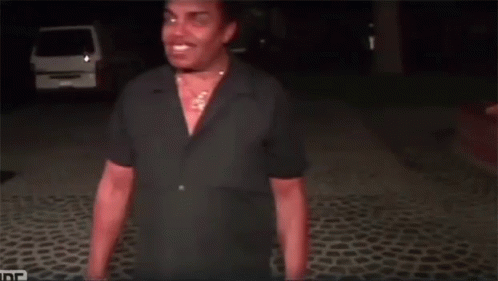 A Man In A Black Shirt Is Standing On A Cobblestone Road GIF