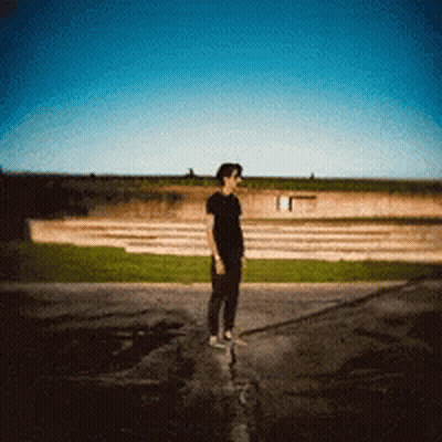 A Man In A Black Shirt Is Standing On A Sidewalk GIF