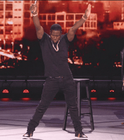 A Man In A Black Shirt Is Standing On A Stage With His Hands In The Air GIF