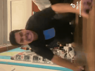 A Man In A Black Shirt Is Standing On A Wooden Floor In A Room With A Blue Wall . GIF