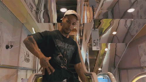 A Man In A Black Shirt Is Standing On An Escalator With A Sign That Says 5F GIF