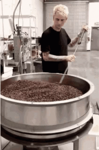 A Man In A Black Shirt Is Stirring A Large Metal Bowl Filled With Beans GIF