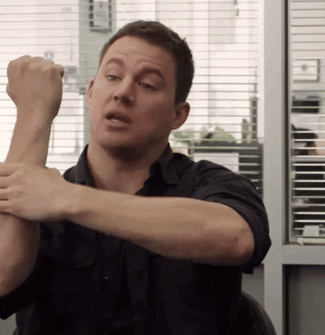 A Man In A Black Shirt Is Stretching His Arms In Front Of A Window GIF