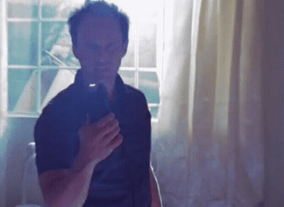 A Man In A Black Shirt Is Taking A Picture Of Himself In Front Of A Window GIF