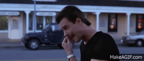 A Man In A Black Shirt Is Talking On A Cell Phone With Makeagif.com At The Bottom GIF
