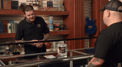 A Man In A Black Shirt Is Talking To Another Man In A Shop GIF
