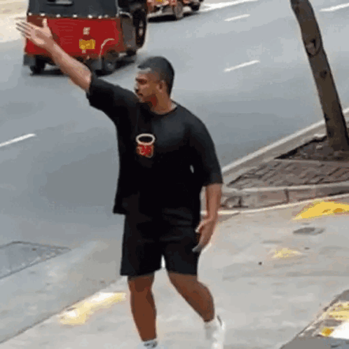 A Man In A Black Shirt Is Walking Down A Sidewalk While A Red Rickshaw Is Driving Behind Him . GIF
