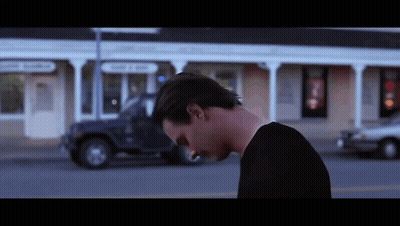 A Man In A Black Shirt Is Walking Down A Street . GIF