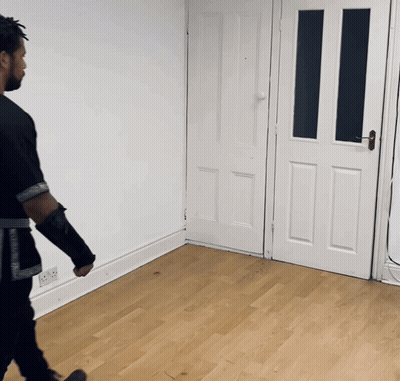 A Man In A Black Shirt Is Walking In A Room With A White Door GIF