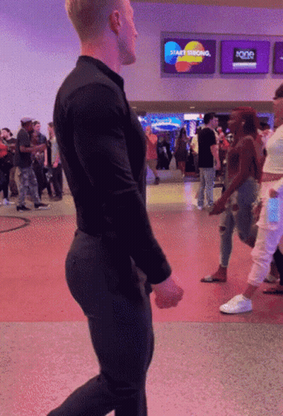 A Man In A Black Shirt Is Walking In Front Of A Sign That Says Start Thinking GIF